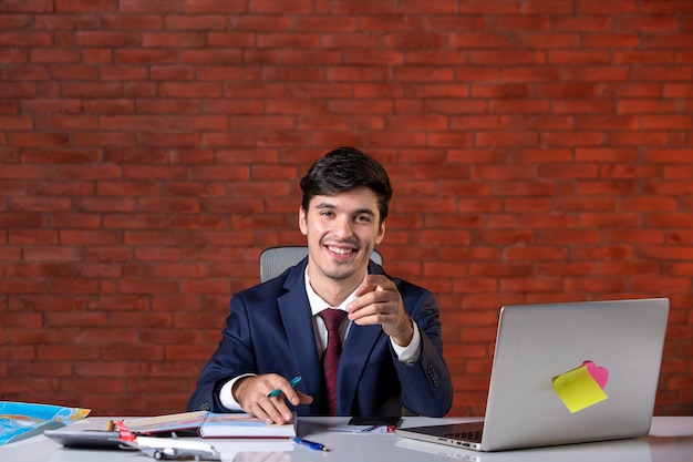 Vorderansicht eines jungen Geschäftsmannes, der hinter seinem Arbeitsplatz mit Laptop im Anzug sitzt Arbeitsplan Auftragnehmer Beruf Baumeister Business Job Corporate Project