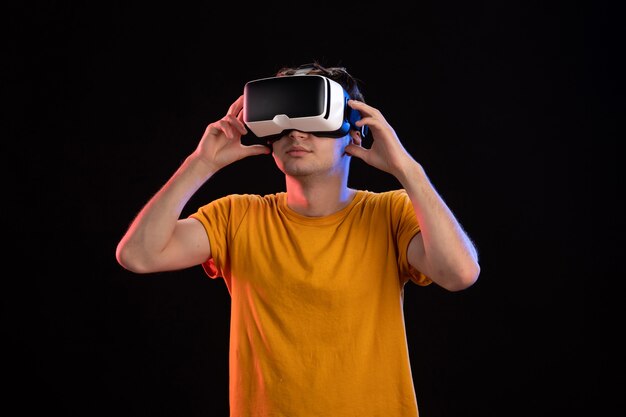 Vorderansicht eines jungen Mannes mit VR-Headset an der dunklen Wand