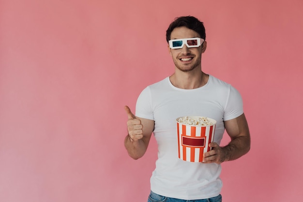 Vorderansicht eines lächelnden, muskulösen Mannes mit 3D-Brille, der Popcorn in der Hand hält und vereinzelt den Daumen nach oben zeigt