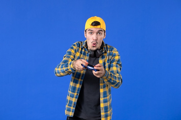 Vorderansicht eines männlichen Spielers mit Gamepad, der Videospiele an blauer Wand spielt