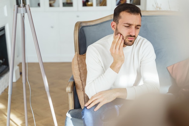 Vorderansicht eines niedergeschlagenen Mannes mit der Hand auf der Wange, der auf einer Couch sitzt