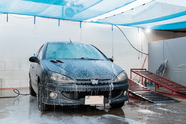 Foto vorderansicht eines schmutzigen autos voller schaum in der autowaschanlage