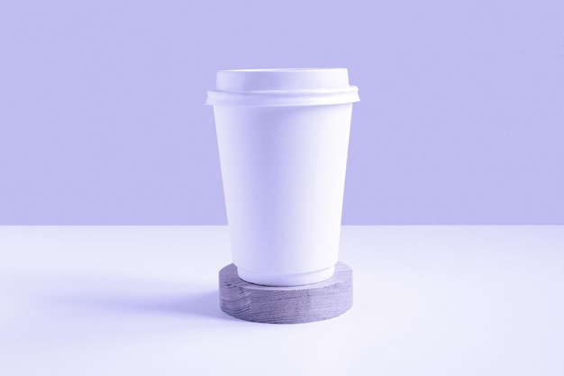Vorderansicht eines weißen Kaffee-Pappbechers Mockup mit Deckel Pappbecher für Kaffee oder Tee auf violettem Hintergrund Zero Waste Plastikfreies Konzept Einweg-Recycling-Becher Holzpodium Sehr peri