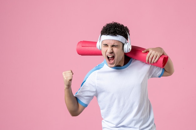 Vorderansicht emotionaler junger Mann in Sportkleidung mit Yogamatte