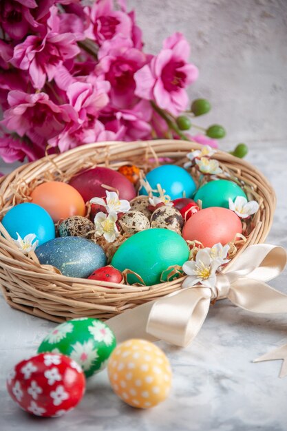 Vorderansicht farbige Ostereier im Korb auf weißer Oberfläche Frühling bunte Osterkonzept Blumenferien verziert