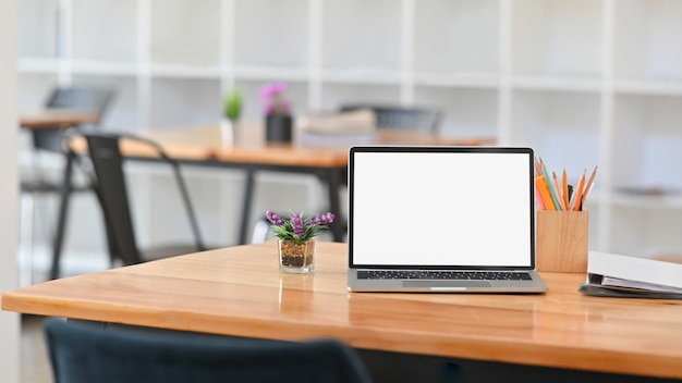 Vorderansicht Foto des weißen leeren Bildschirmlaptops auf dem Schreibtisch. Inklusive Stifthalter, Dokumentenakten und Topfpflanze auf dem Schreibtisch.