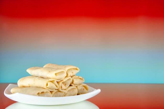 Vorderansicht gerollte süße Pfannkuchen im Teller auf hellrotem Hintergrund Essen Frühstück Zucker Milch Morgenkuchen Farbe Mahlzeit