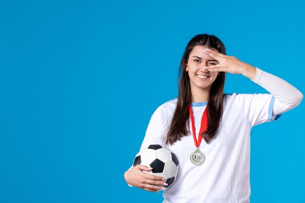 Vorderansicht junge Frau, die Fußball auf blauer Wand hält