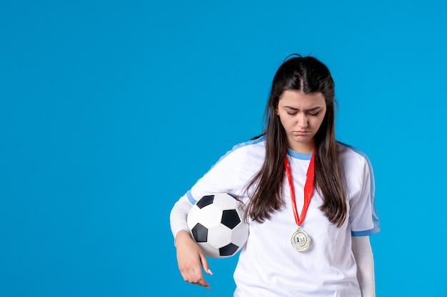 Vorderansicht junge Frau, die Fußball auf blauer Wand hält