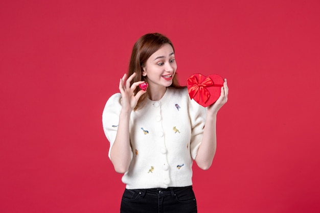 Vorderansicht junge Frau, die rotes herzförmiges Geschenk auf rotem Hintergrund hält Frauentag, der sinnliche weibliche Liebe Modegleichheit einkauft