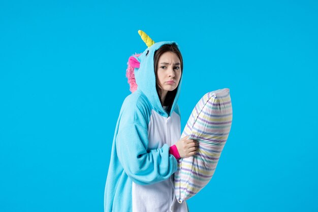 Vorderansicht junge Frau in Kigurumi für Pyjama-Party mit Kissen auf blauem Hintergrund Cartoon Traum Schlaf Freunde Spielnacht Spaß Farbe Anime Bett