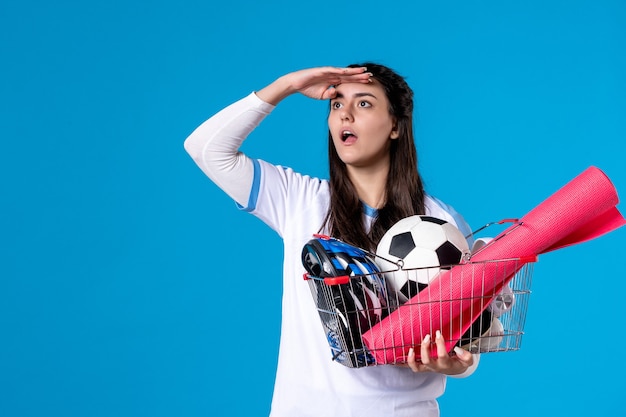 Vorderansicht junge Frau mit Korb voller Sport Dinge, die Entfernung blaue Wand betrachten