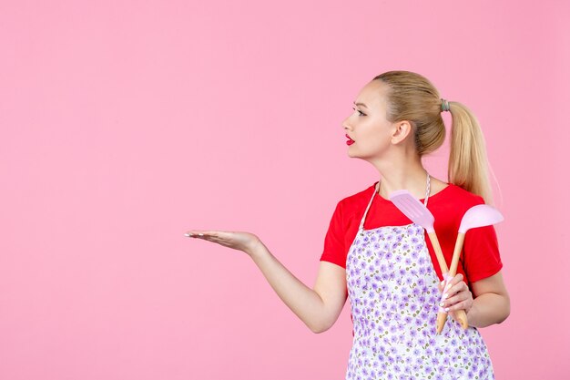 Vorderansicht junge Hausfrau mit Besteck an rosa Wand