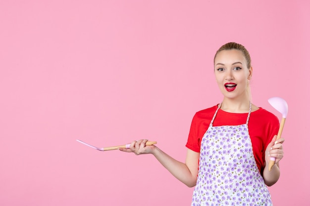 Vorderansicht junge Hausfrau mit Besteck an rosa Wand