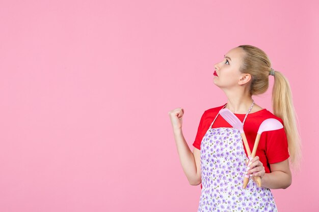 Vorderansicht junge Hausfrau mit Besteck an rosa Wand