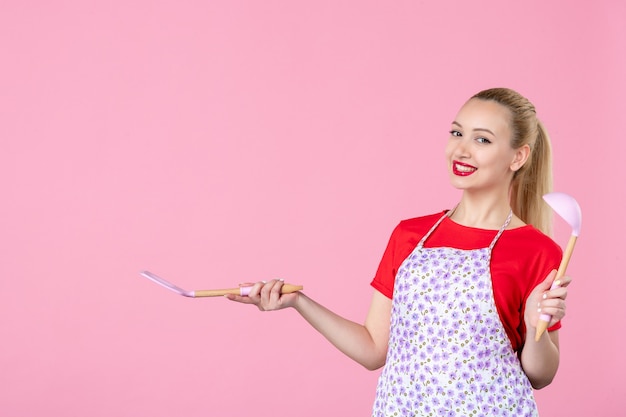 Vorderansicht junge Hausfrau mit Besteck an rosa Wand