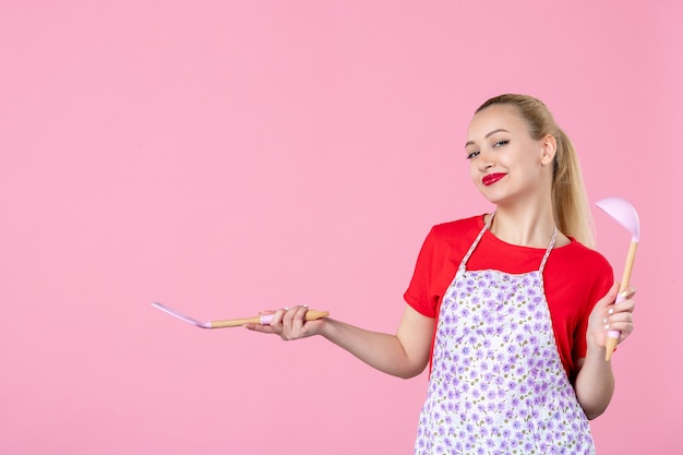Vorderansicht junge Hausfrau mit Besteck an rosa Wand