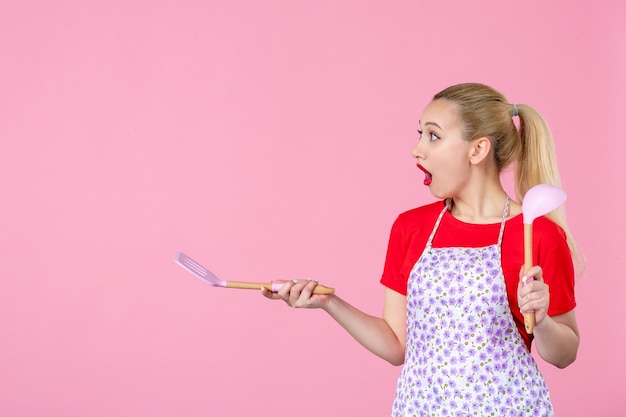 Vorderansicht junge Hausfrau mit Besteck an rosa Wand