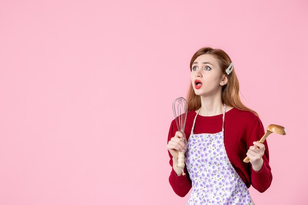 Vorderansicht junge Hausfrau mit Löffel und Schneebesen auf rosa Hintergrund süße Farbe Küche Essen Kuchen Kuchen Küche Teig kochen