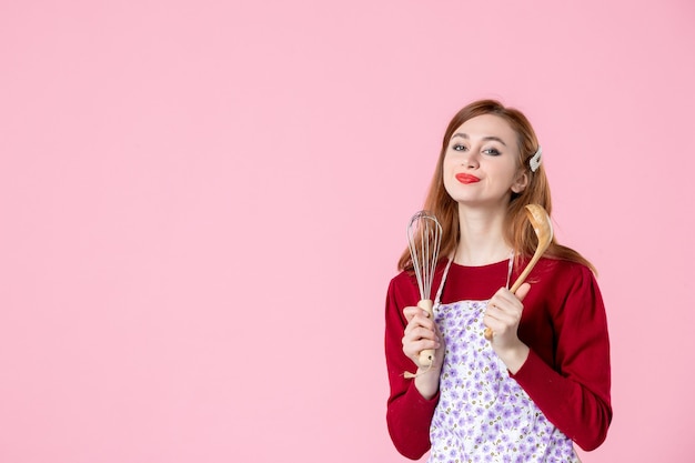 Vorderansicht junge Hausfrau mit Löffel und Schneebesen auf rosa Hintergrundfarbe Kochen Kuchen Küche Küche süße Teig Essen Frau Kuchen