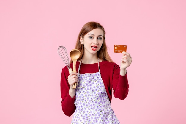 Vorderansicht junge Hausfrau mit Schneebesen und Bankkarte auf rosa Hintergrund Küche Kuchen Kuchen Frau Farbe Einkaufen Kochen Geld Küche Essen