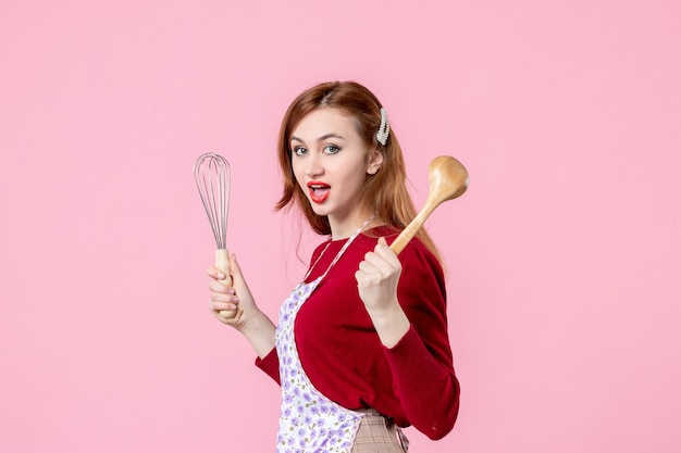 Vorderansicht junge Hausfrau mit Schneebesen und Holzlöffel auf rosa Hintergrund kochen Teig horizontale einheitliche Beruf Frau Kuchen Küche