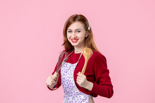Vorderansicht junge Hausfrau mit Schneebesen und Holzlöffel auf rosa Hintergrund kochen Teig horizontale Torte Beruf Frau Kuchen Küche