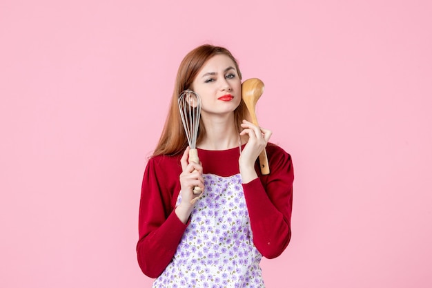 Vorderansicht junge Hausfrau posiert mit Schneebesen und Holzlöffel auf rosa Hintergrund Kuchen Beruf Kochen einheitlicher horizontaler Kuchen Küche Teig