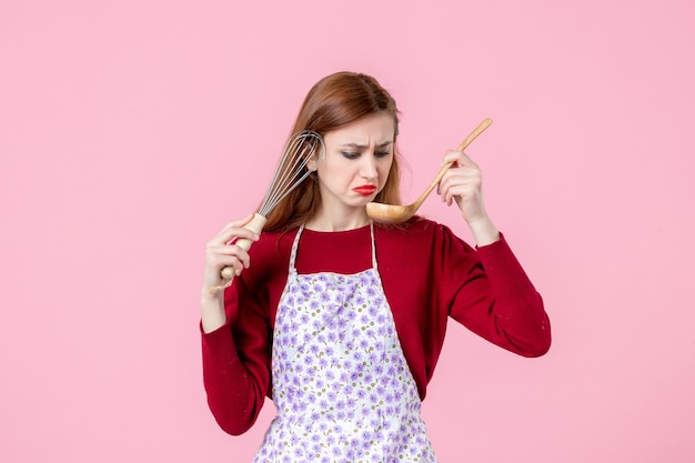 Vorderansicht junge Hausfrau posiert mit Schneebesen und Holzlöffel auf rosa Hintergrund Kuchen Beruf Kochen Teig Frau einheitliche horizontale Kuchen Küche
