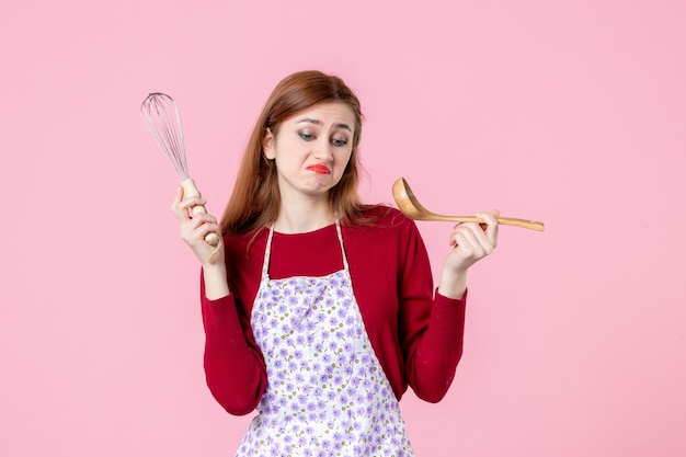 Vorderansicht junge Hausfrau posiert mit Schneebesen und Holzlöffel auf rosa Hintergrund Kuchen Beruf Kochen Teig horizontale Torte Küche Frau