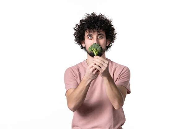 Vorderansicht junger Mann, der kleinen grünen Brokkoli auf weißem Hintergrund hält Körpergesundheit Diät Gewicht Salat menschliches Gemüse