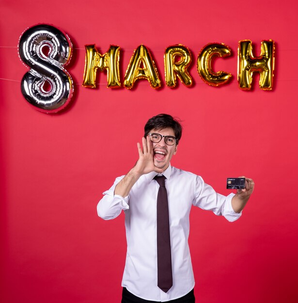 Vorderansicht junger Mann, der schwarze Bankkarte auf rotem Hintergrund hält Shopping-Vogue-Farbe sinnlicher Womans Tag März Geld Urlaub präsentiert