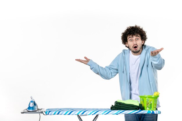 Vorderansicht junger Mann hinter Bügelbrett auf weißem Hintergrund Farbe Mann Reinigung Hausarbeit Wäsche Foto Bügeleisen Kleidung