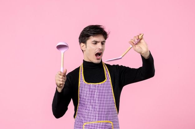 Vorderansicht junger Mann im Kap mit Löffeln auf rosa Hintergrundfarbe Essen kochen horizontale Arbeit Teig Küche Beruf