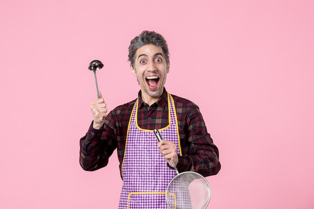 Vorderansicht junger Mann im Kap mit Sieb und Löffel auf rosa Hintergrund Essen Küche Ehemann horizontaler Beruf einheitlicher Küchenarbeiter Koch