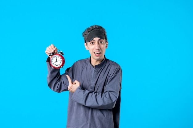 Vorderansicht junger Mann im Pyjama, der rote Uhren auf blauem Hintergrund hält dunkle Albtraumfarbe Schlaf spät träumen Nacht Bettzeit