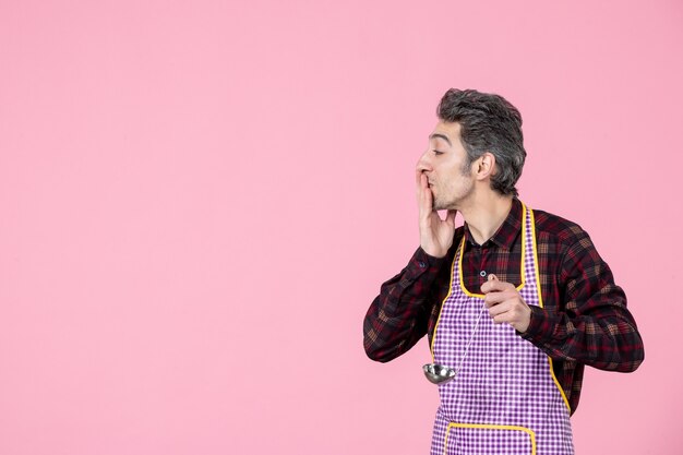 Vorderansicht junger Mann im Umhang mit silbernem Suppenlöffel auf rosa Hintergrund Küche Arbeiter Ehemann Küche Koch horizontaler Beruf