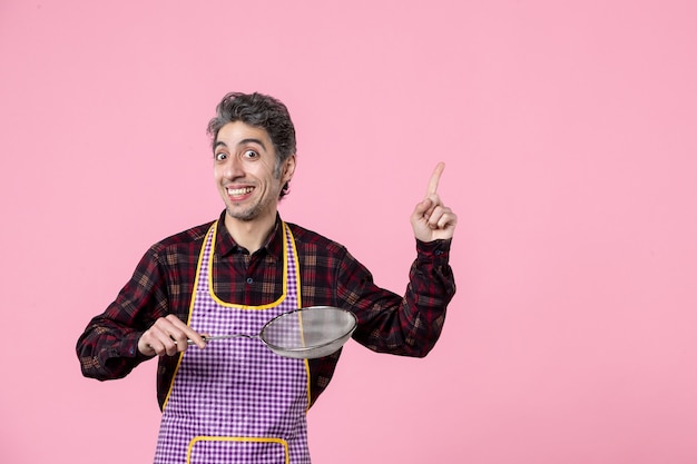 Vorderansicht junger Mann in Cape mit Sieb auf rosa Hintergrund Job Beruf Ehemann Küche Koch Farbe horizontale Lebensmittelarbeiterin