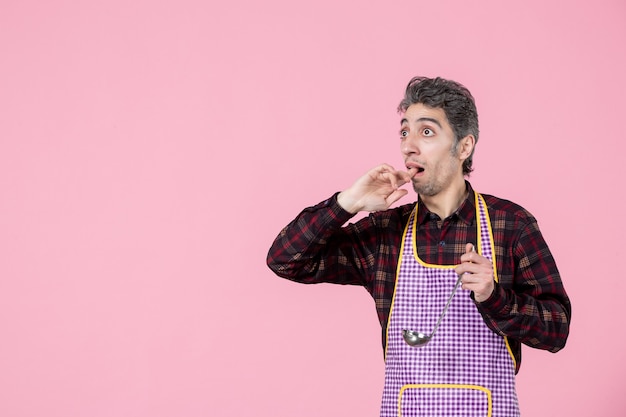 Vorderansicht junger Mann in Cape mit Suppenlöffel und Blick auf etwas rosa Hintergrund Job Beruf horizontaler Koch Arbeiter Essen Ehemann Küche