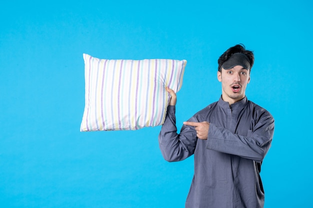Vorderansicht junger Mann in seinem Pyjama, der Kissen auf blauem Hintergrund hält Albtraum Ruhe Traum spät Farbe aufwachen menschlichen Schlaf Bett