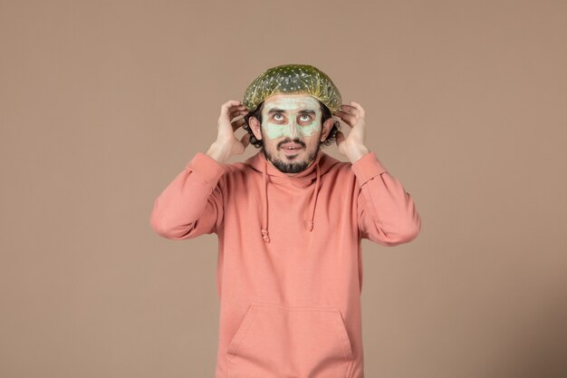 Vorderansicht junger Mann mit bauschiger Mütze und Maske auf seinem Gesicht auf braunem Hintergrund Hautpflege-Therapie-Haar-Gesichts-Spa-Haut