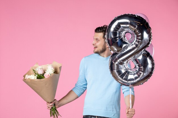 Vorderansicht junger Mann mit Blumen und Luftballons als März auf rosa Hintergrund vorhanden Gleichheit Ehe Liebe horizontaler Frauentag sinnliches Datum