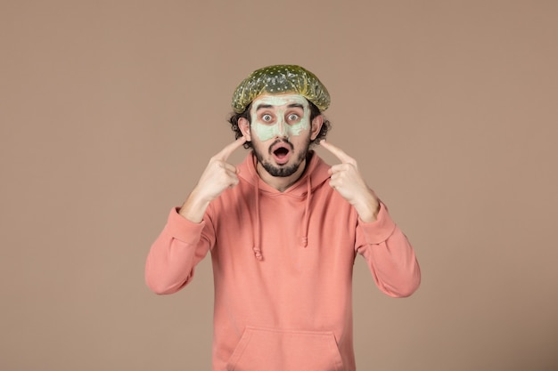 Vorderansicht junger Mann mit Bouffant-Kappe und Maske auf seinem Gesicht auf braunem Hintergrund Salonfarbe Hautpflege-Therapie Haargesichts-Spa-Haut