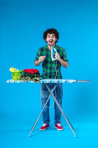 Vorderansicht junger Mann mit Bügelbrett mit Bügeleisen auf blauem Hintergrund Farbe Haus Waschmaschine menschliche Kleidung Hausarbeit