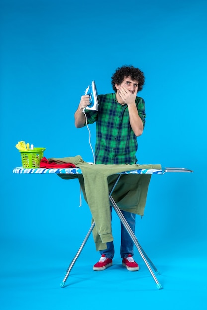 Vorderansicht junger Mann mit Bügeleisen auf blauem Hintergrund saubere Waschmaschine Farbe menschliche Hausarbeit