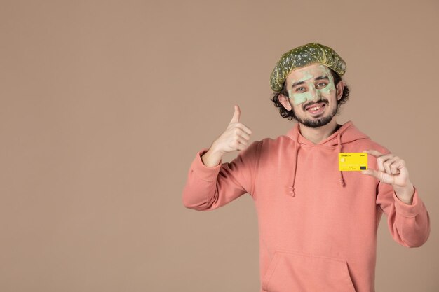 Vorderansicht junger Mann mit gelber Kreditkarte auf braunem Hintergrund Spa-Körperpflege-Therapie Hautpflege-Salon Gesichtshaut
