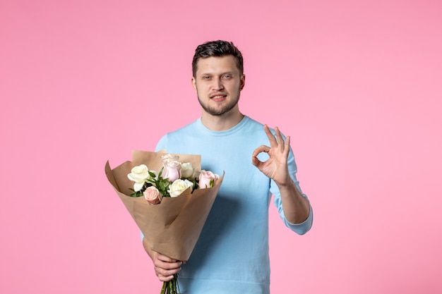 Vorderansicht junger Mann mit Strauß schöner Blumen auf rosa Hintergrund Spaßpark sinnlicher Frauentag März weibliches Datum Gleichheit der Ehe Liebe