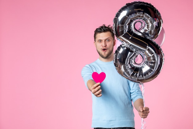 Vorderansicht junger Mann mit süßen Luftballons und Herzaufkleber auf rosa Hintergrund Liebe weiblicher Frauentag Ehegleichheit Datum März sinnlicher Spaß