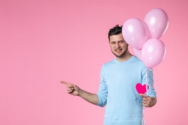 Vorderansicht junger Mann mit süßen rosa Luftballons und Herzaufkleber auf rosa Hintergrund Gleichheit Frauentag Ehe Marsch sinnlich weiblicher Spaß Liebespark