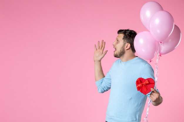 Vorderansicht junger Mann mit süßen rosa Luftballons und herzförmigem Geschenk auf rosa Hintergrund Liebe sinnliche Gleichheit Frauentag Ehe Marsch weiblicher Parkspaß